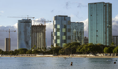 Modern buildings by river against sky in city