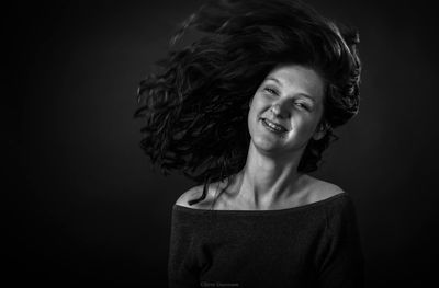 Portrait of smiling young woman against black background