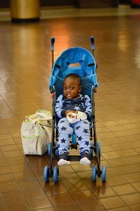 Portrait of cute toddler in baby stroller over tiled floor