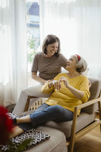 Smiling woman sitting on chair with elderly mother-in-law at home