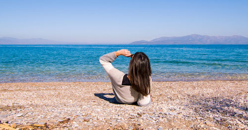 Woman sitting on shore at sea against sky