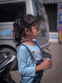 Cute girl looking away while standing by car