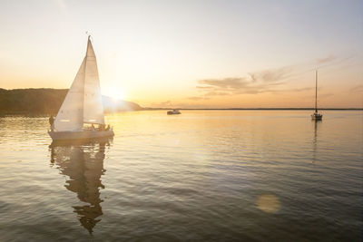 Sailboats in sea against sky during sunset