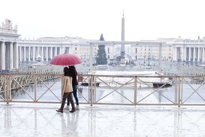 Couple walking on walkway against st peter square during rainy season
