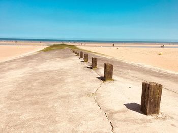 Wooden posts on beach against clear blue sky