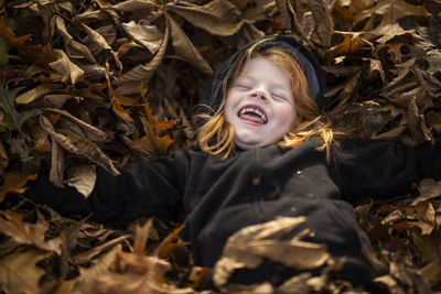 High angle view of cheerful girl lying on fallen autumn leaves