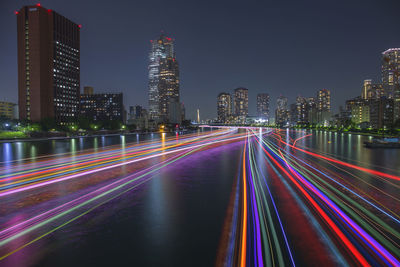 Light trails on illuminated buildings against sky at night