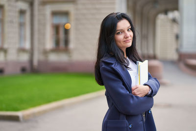 Portrait of young woman holding books outside university