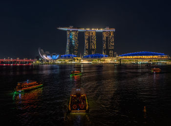 Illuminated marina bay sands by river against clear sky at night