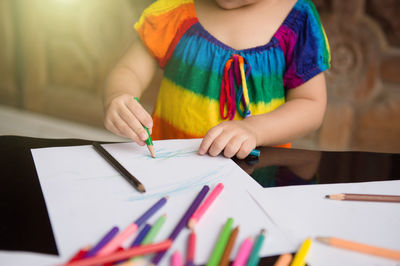 Low section of woman holding paper with pencils on table