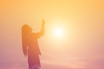 Silhouette woman standing against bright sun during sunset