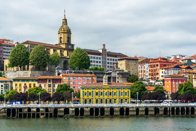 Buildings in river against cloudy sky