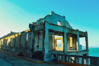 Abandoned building by sea against clear blue sky