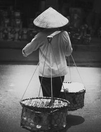 Rear view of man carrying baskets on shoulder at market