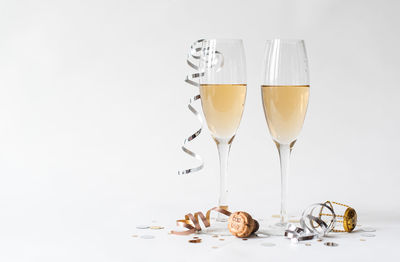 Two glasses of champagne, cork, ribbon and confetti on white backdrop.