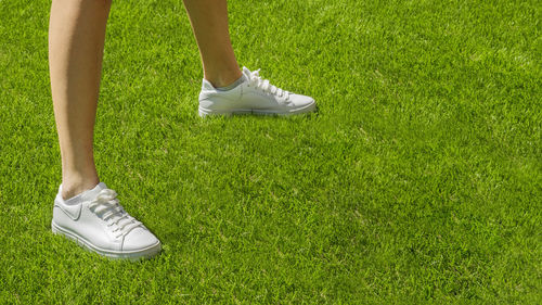 Female legs in white sneakers on a background on a green sports field. 