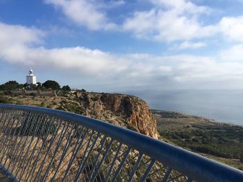 Bridge railing by cliff against cloudy sky