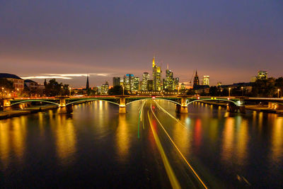 Illuminated bridge over river amidst buildings in city at night