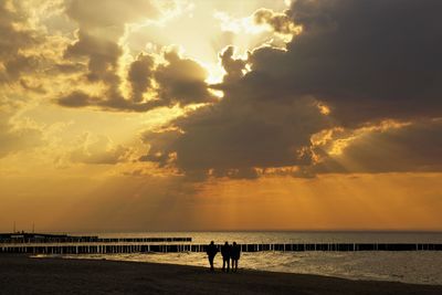 Silhouette people on beach against sky during sunset