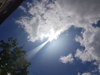 Low angle view of sunlight streaming through clouds