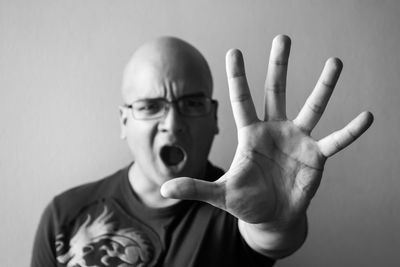 Portrait of angry bald man showing hand while shouting against wall