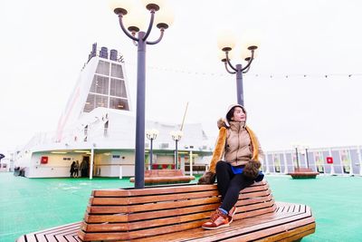 Full length of woman sitting on bench in city