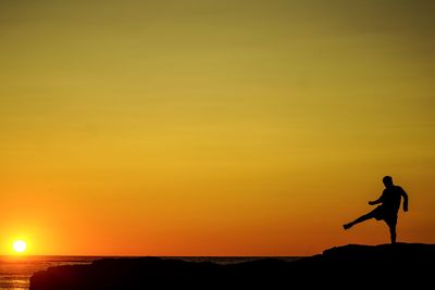 Silhouette man standing on rock against sky during sunset