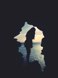 Silhouette people standing on rock by sea against sky during sunset