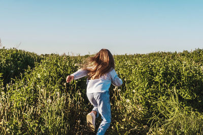 Rear view of girl running on land against clear sky