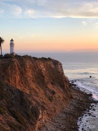 Lighthouse on beach against sky during sunset