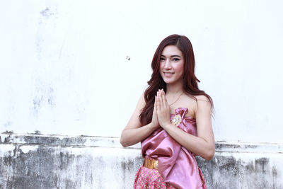 Portrait of smiling young woman standing against wall