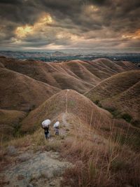 Rear view of man walking on field against sky during sunset