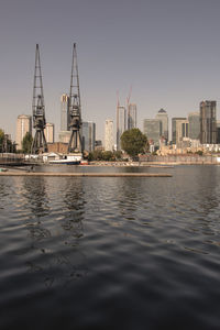 Sailboats in river by buildings against sky