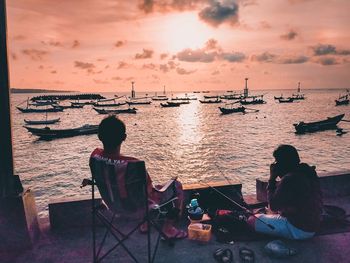 Rear view of people sitting on beach against sky during sunset