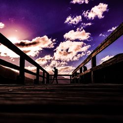 Silhouette man on footbridge against sky during sunset