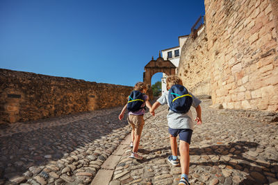 Rear view of people walking on street against clear blue sky