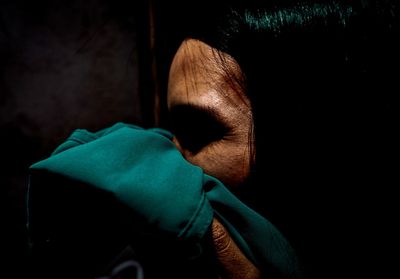 Close-up of woman covering mouth with green fabric in darkroom