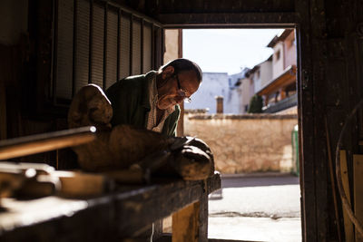 Senior woodworker in glasses working with piece of lumber in workshop