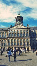 People walking in front of buildings in city against sky