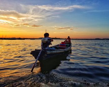 Man on boat in sea against sky during sunset