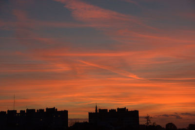 Silhouette of city against cloudy sky during sunset