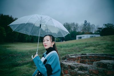 Woman holding umbrella while standing on field