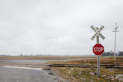Railroad crossing sign on road against cloudy sky