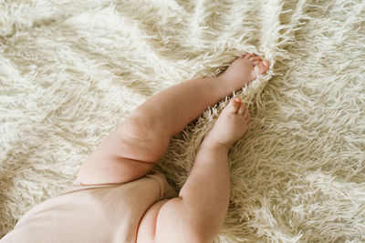 Belly and legs of a newborn baby in a bodysuit lying on a light bed, top view