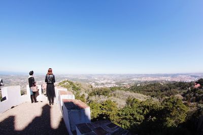 People standing on landscape against clear blue sky