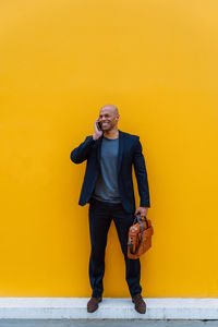 Portrait of young man standing against yellow wall