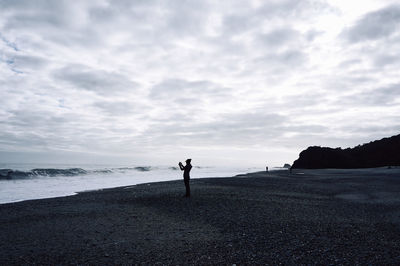 Silhouette person standing at beach against cloudy sky at dusk