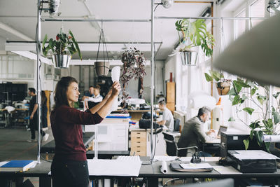 Mid adult businesswoman examining paper while colleagues working in background at creative office