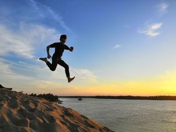 Man jumping in sea against sky during sunset