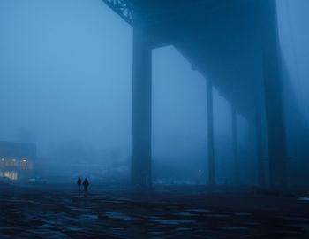Rear view of man walking in foggy weather against sky during winter